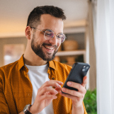 Ein CED-Patient steht in seinem Wohnzimmer und betrachtet seinen Calprotectin-Wert auf dem Smartphone.