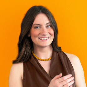 Portrait einer jungen laechelnden Frau mit braunen Haaren auf orangenem Hintergrund.