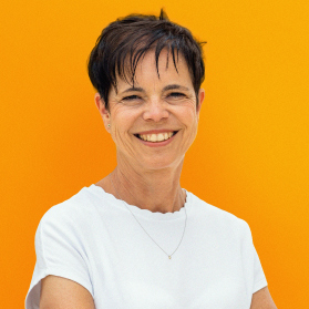 Portrait einer laechelnden Frau mit kurzen schwarzen Haaren auf orangenem Hintergrund.