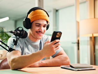 Content Creator nimmt einen Podcast auf und betrachtet ein Testergebnis auf seinem Smartphone.