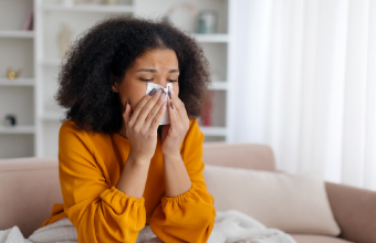 A woman has an infectious illness, such as the flu or influenza, and blows her nose with a tissue.
